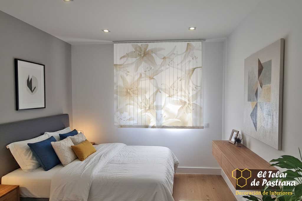 Recámara: cortina vertical con impresión digital de lirios blancos, cama con ropa de cama blanca, cabecero gris y mueble flotante de madera.