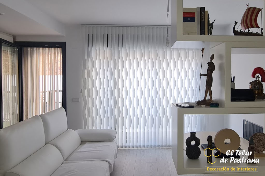 Sala de estar: cortina vertical blanca con ondas, sofá blanco, estantería divisoria blanca con decoraciones y suelo de madera clara.