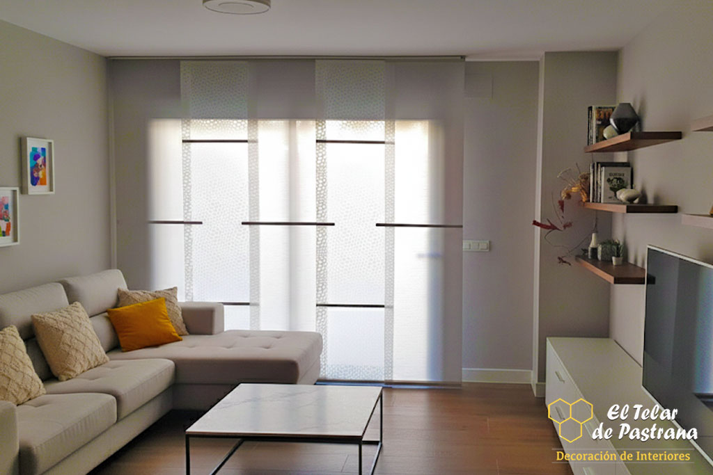 Cortina vertical blanca y beige con topping, salón comedor, mesa madera rectangular, sofá chaise longue gris.