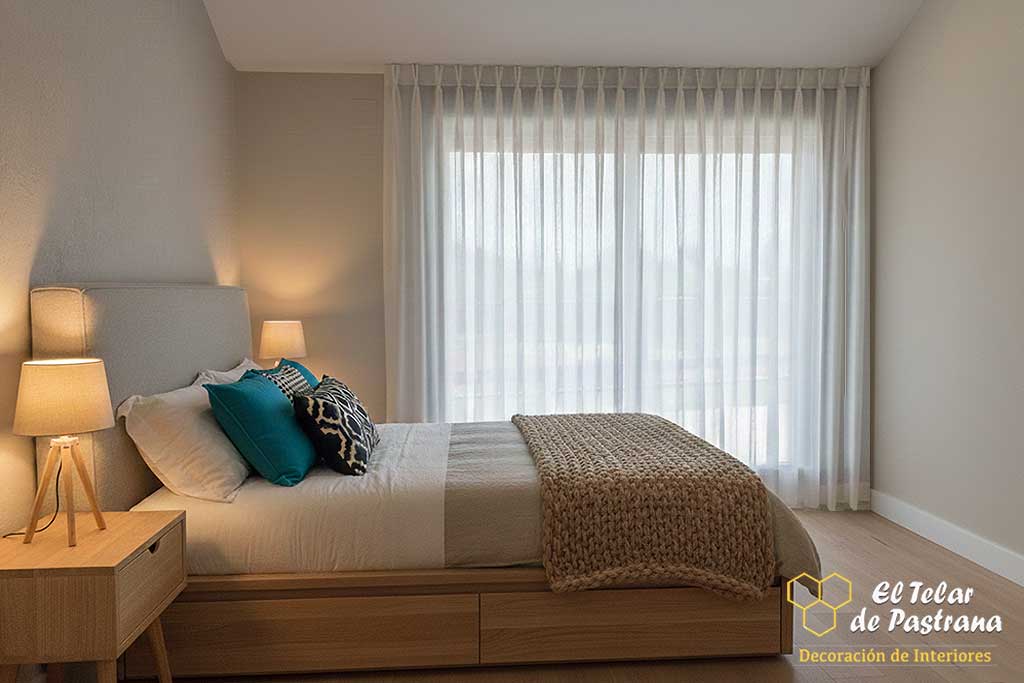 Dormitorio neutro con cama de madera clara y visillo de gran caída con pinza pliegue