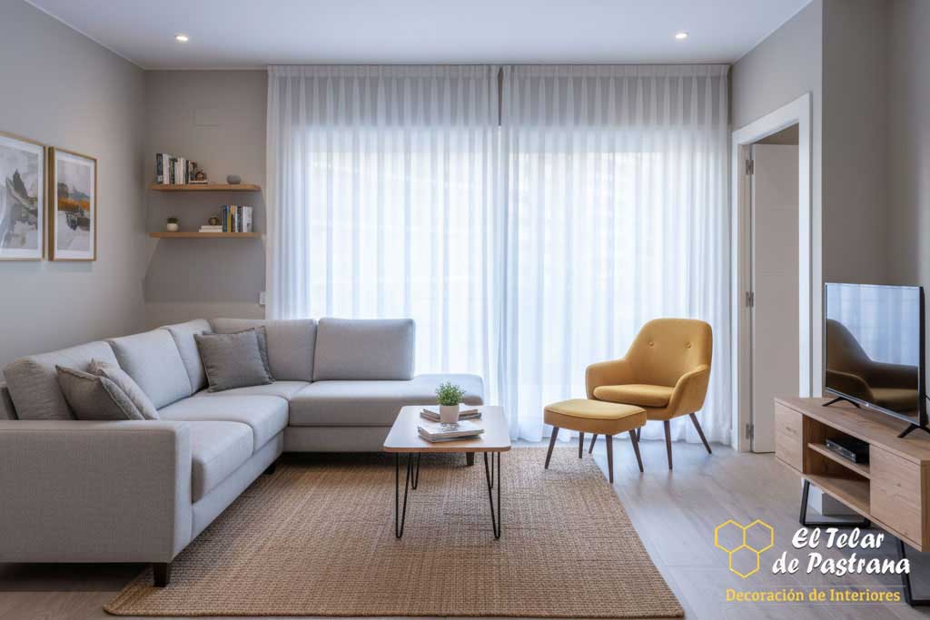 Salón moderno con visillo de pinza pliegue, sofá modular gris, butaca amarilla y mesa de centro de diseño con patas de metal.