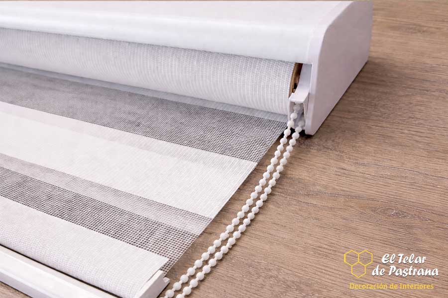 BeneficiDetalle del tejido de un estor noche y día en color blanco con sistema de cadena y cajón superior para control de luz y privacidados de los estores noche y día en screen