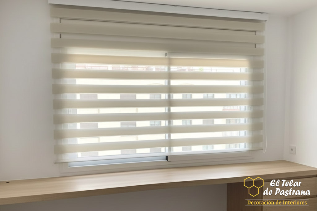 Estor noche y día en tono beige instalado en ventana de despacho con mesa de trabajo, regulando la entrada de luz natural