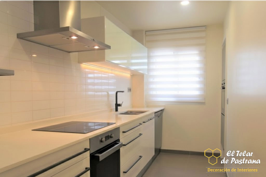 Cocina moderna y luminosa con estor noche y día blanco instalado en ventana, muebles blancos y control de la luz natural