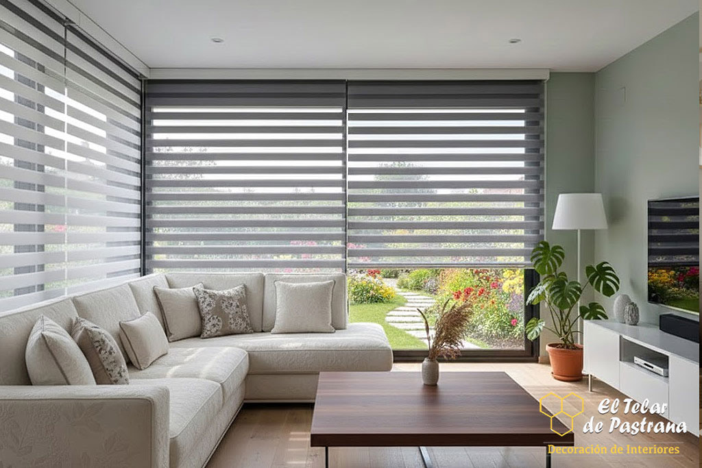 Salón amplio y luminoso con estores noche y día en tonos gris y blanco instalados en grandes ventanales, sofá en esquina y vistas al jardín