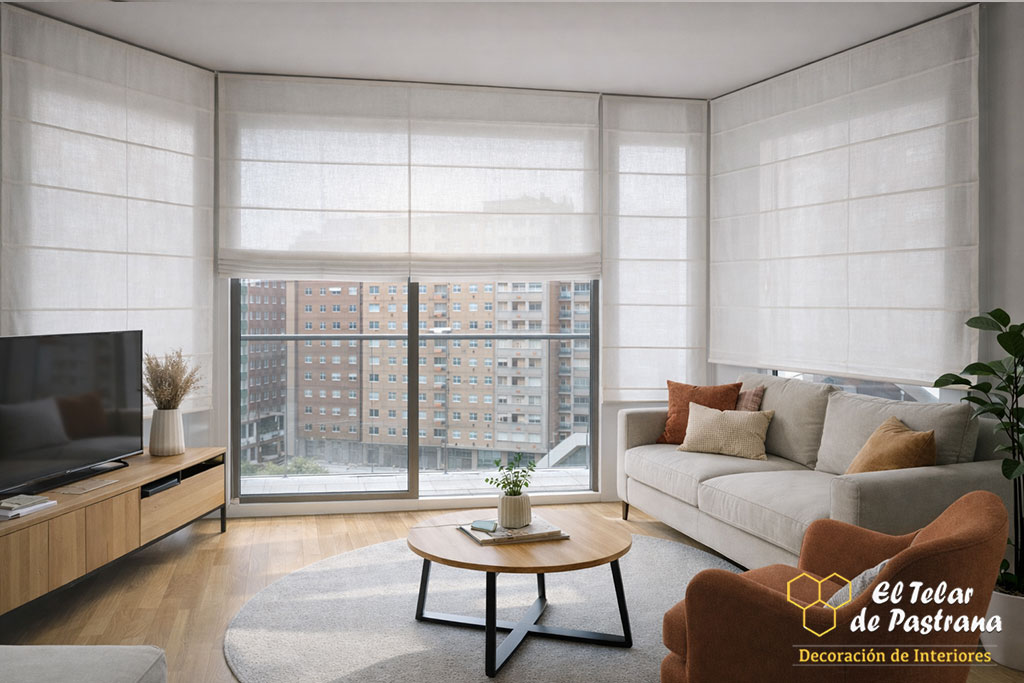 Salón luminoso con sofá, mesa de centro y estores plegables blancos instalados en grandes ventanales curvos