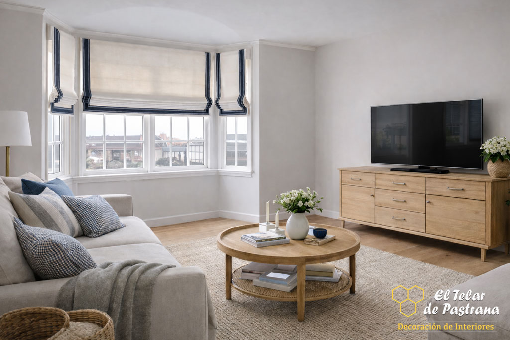 Salón elegante con sofá claro, mesa de centro de madera y estores plegables a cenefa instalados en ventanal curvo